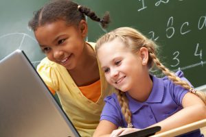 Portrait of two schoolgirls looking at the laptop during lesson